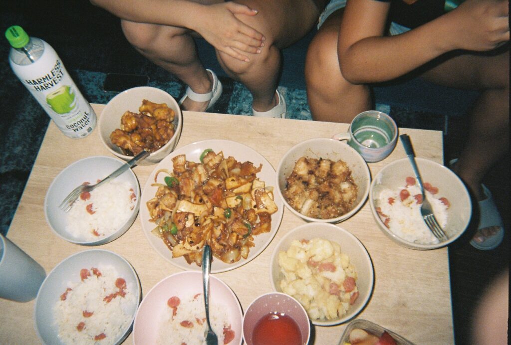 Table of dishes with food, some eaten, utensils in dishes, lower half of two people on opposite side of table sitting down