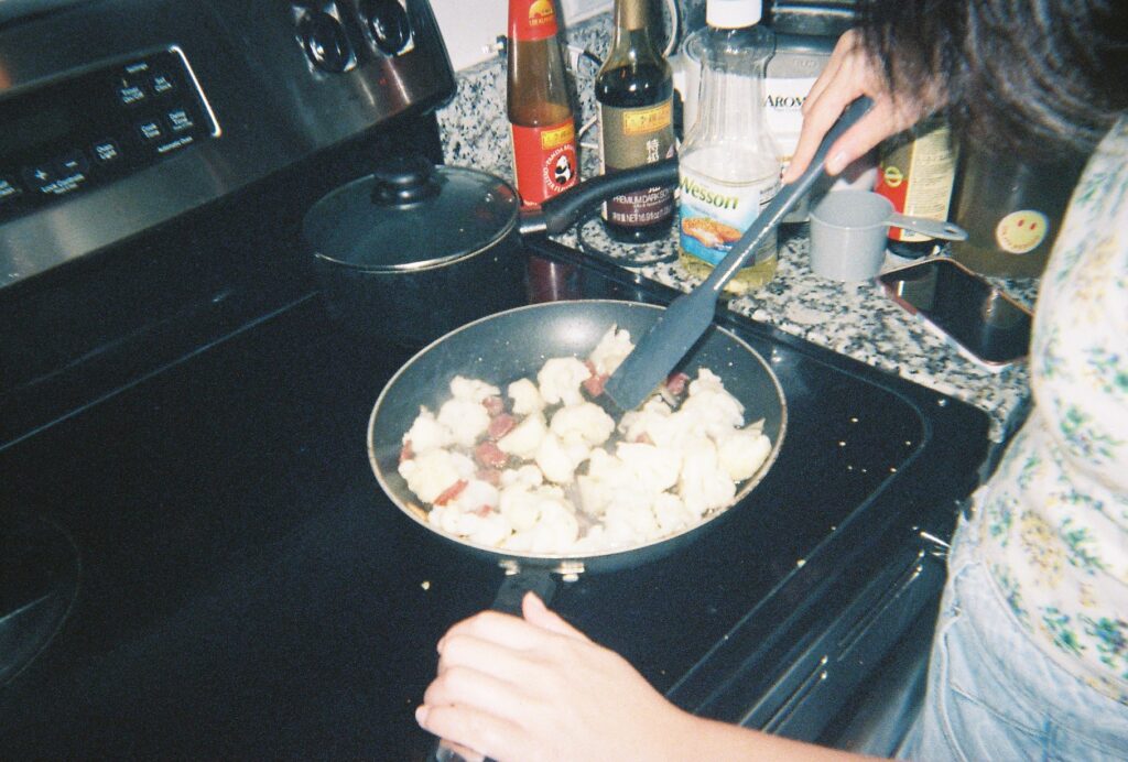 Person suateeing foot on stove one hand on handle and one hand stirring what's being cooked with sauces on counter to right