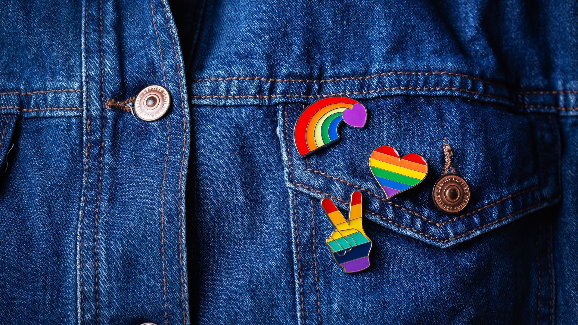 Close up of a denim jacket on a person with Pride buttons over left chest pocket