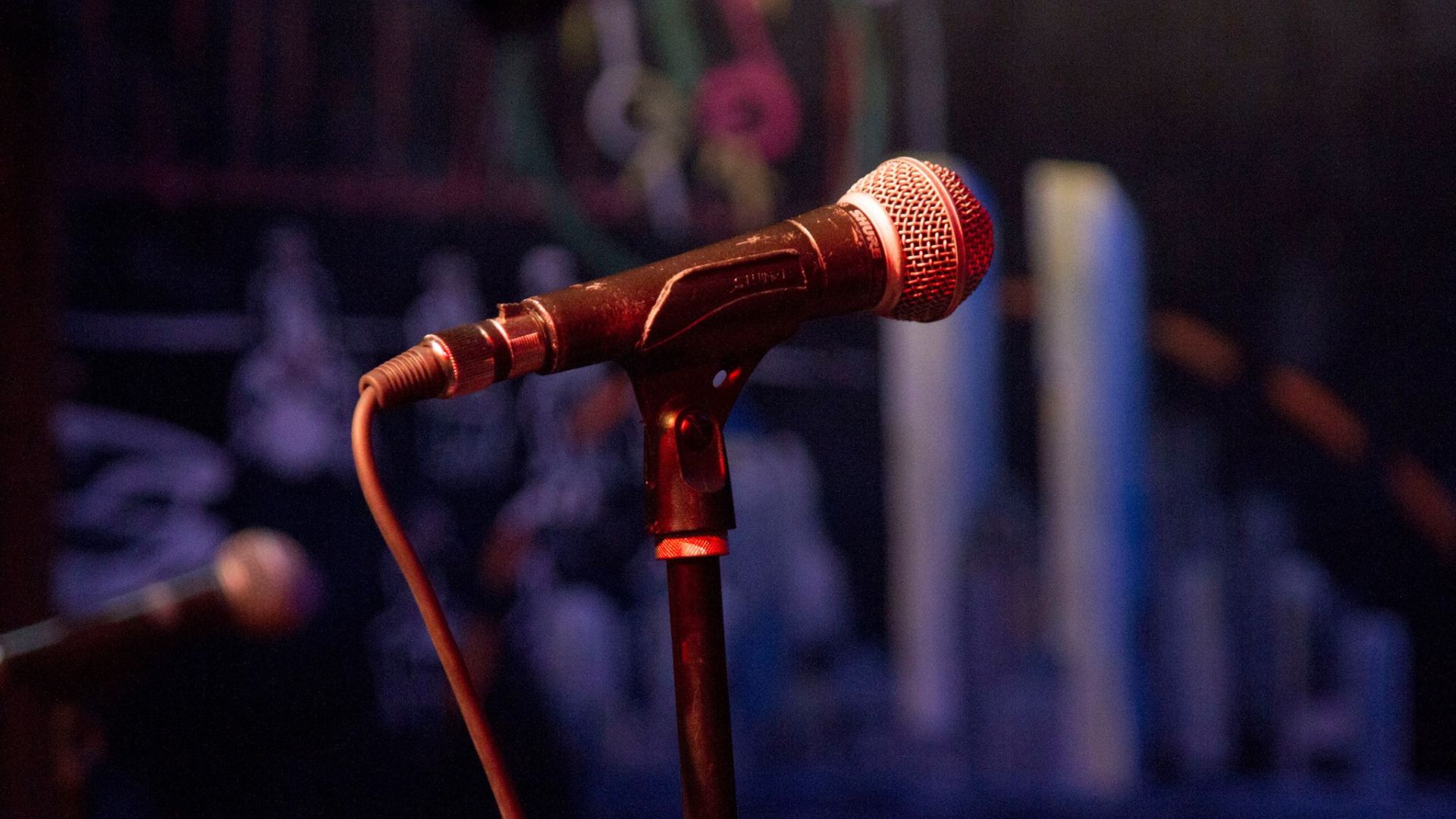 A closeup of a microphone on a stage, with a dark blue graffitied wall behind it.